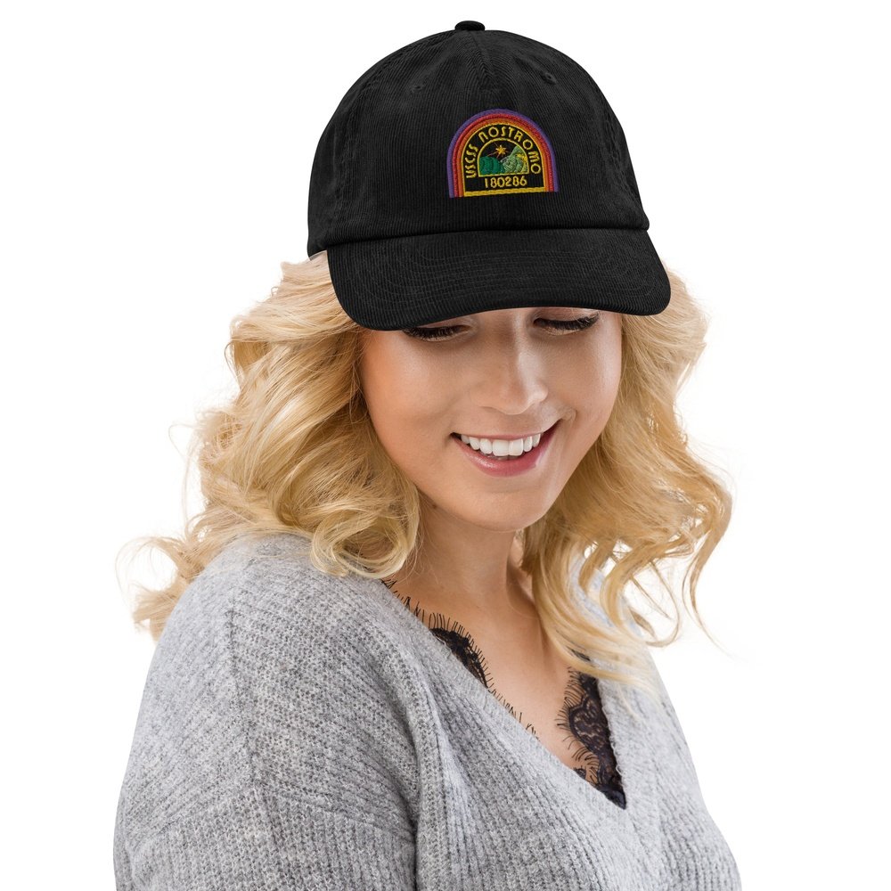 A person wearing a black Alien USCSS Nostromo embroidered dad hat featuring a rainbow-style logo on the front.