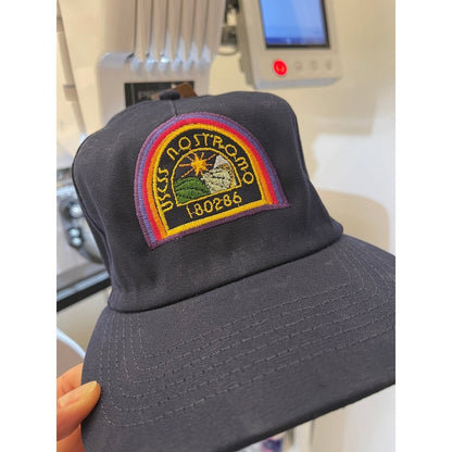 A black Alien USCSS Nostromo embroidered dad hat features a rainbow-style logo with the ship's name and the number 180288 displayed prominently on the front.