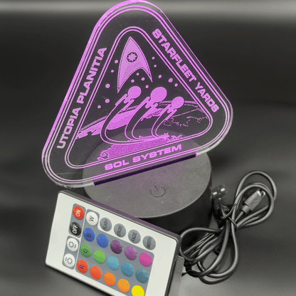 An LED engraved acrylic lamp depicts a Starfleet shipyard scene from Utopia Planitia, labeled "Utopia Planitia Shipyard" and "Sol System," accompanied by a remote control for color adjustment.