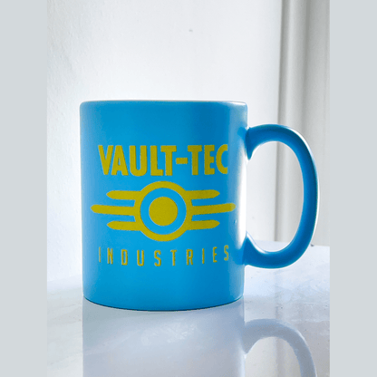 A blue matte mug displays the Vault-Tec Industries logo in yellow lettering and a circular emblem referencing the Fallout video game series.