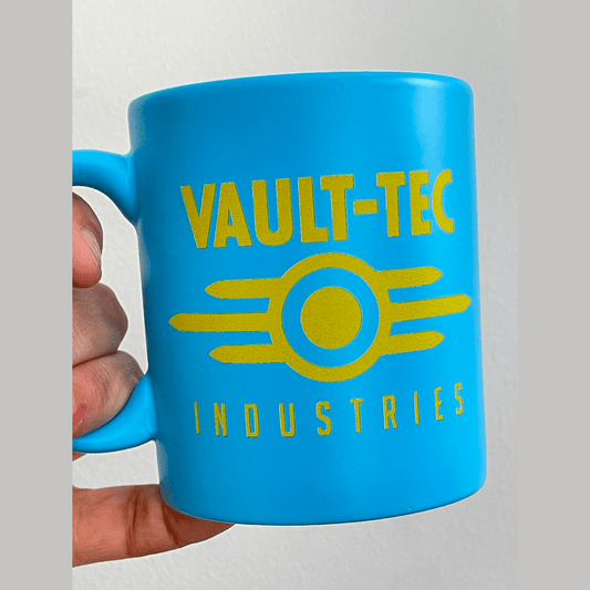 A blue Fallout mug displays the yellow Vault-Tec Industries logo.