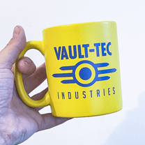 A hand holds a yellow mug displaying the Vault-Tec Industries logo from the Fallout video game series.