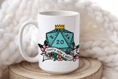 A white mug displays a D&D-themed design featuring a twenty-sided die (d20) surrounded by flowers and the phrase "That's How I Roll.