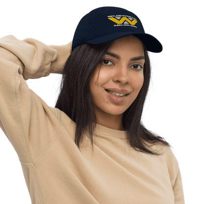 A person wearing a navy blue baseball cap embroidered with the Weyland-Yutani Corp logo smiles while holding up their hair.