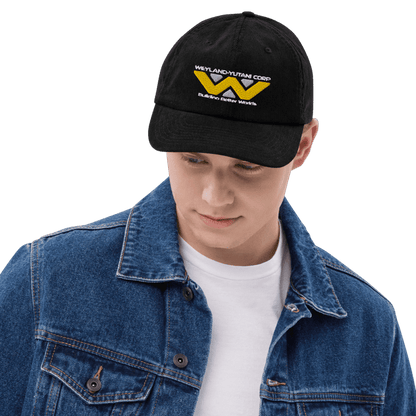 A person wearing a black baseball cap embroidered with the Weyland-Yutani Corp logo from Alien.