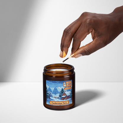 A hand lights a Stardew Valley scented candle featuring an illustration of Featherstone Farm on its label.