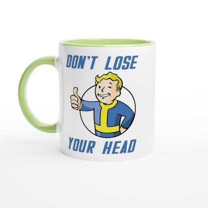A white mug with a green handle features Vault-Tec branding and cartoon character giving a thumbs up alongside the text "Don't Lose Your Head," referencing the Fallout video game series.
