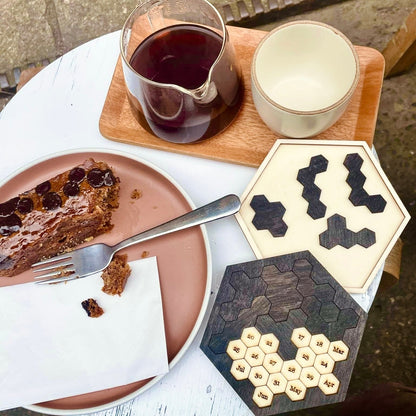 A wooden tray displays a slice of chocolate cake, a glass pitcher of liquid, and two Star Trek inspired puzzles featuring wooden hexomino pieces and a date puzzle with numbered segments.