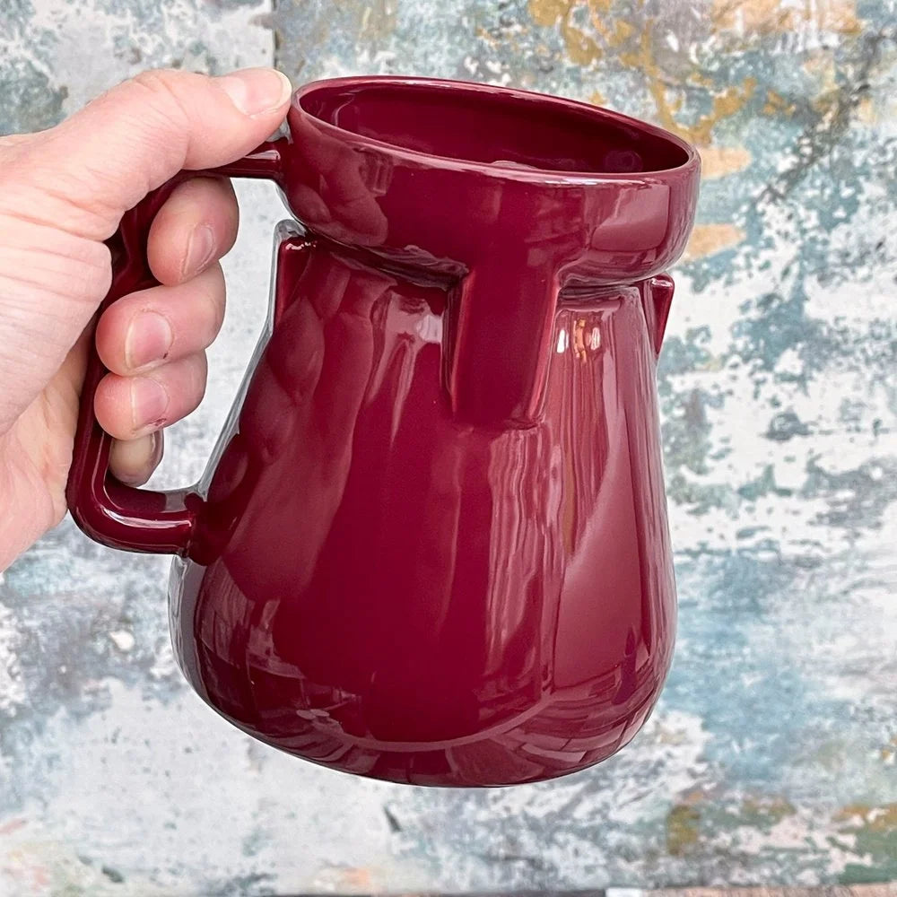 A hand holds a deep red Raktajino replica mug inspired by Big Red Synth Ale from Quark's Bar in DS9.