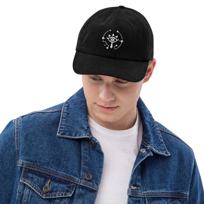 A person wearing a black Zelda Sheikah embroidered dad hat featuring a white eye design inspired by Tears of the Kingdom.
