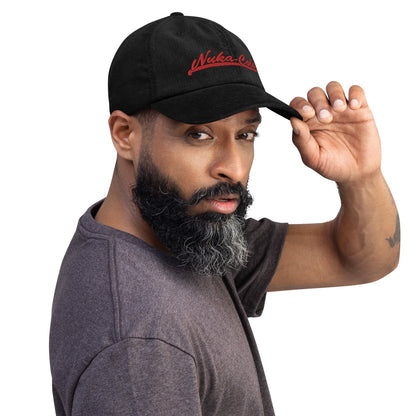 A man wearing a black Nuka Cola Red Embroidered Dad Hat shields his eyes with his hand.