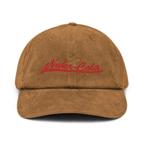 A brown corduroy dad hat features red embroidered "Nuka Cola" lettering across the front.