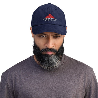 A person wearing a dark blue baseball cap featuring the Cyberdyne Systems logo embroidered on the front.