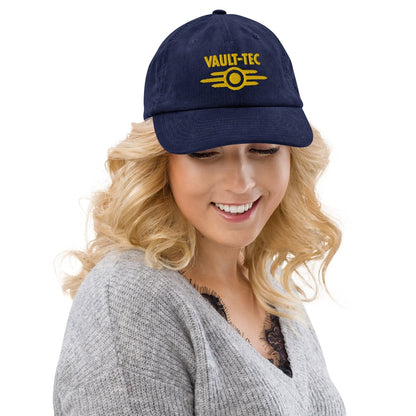 A woman wearing a blue Vault-Tec baseball cap featuring yellow embroidered lettering and a logo from the Fallout video game series.