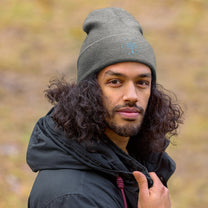 A person wearing a grey Zelda Sheikah embroidered beanie with a glow-in-the-dark design stands against an out-of-focus background.