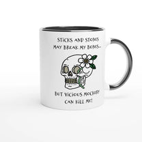 A white ceramic mug with a black rim features a drawing of a skull adorned with flowers and the phrase "Sticks and Stones May Break My Bones... But Vicious Mockery Can Kill Me!