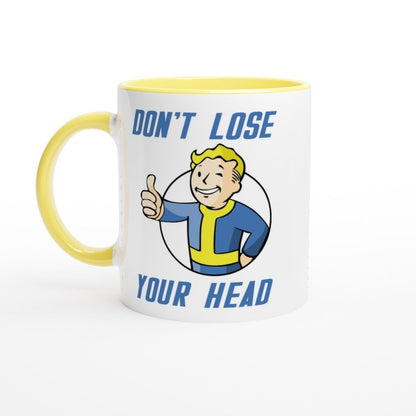 A white mug with a yellow handle and rim features Vault-Tec branding and cartoon artwork reading "Don't Lose Your Head" alongside a character giving a thumbs up, referencing the Fallout video game series.