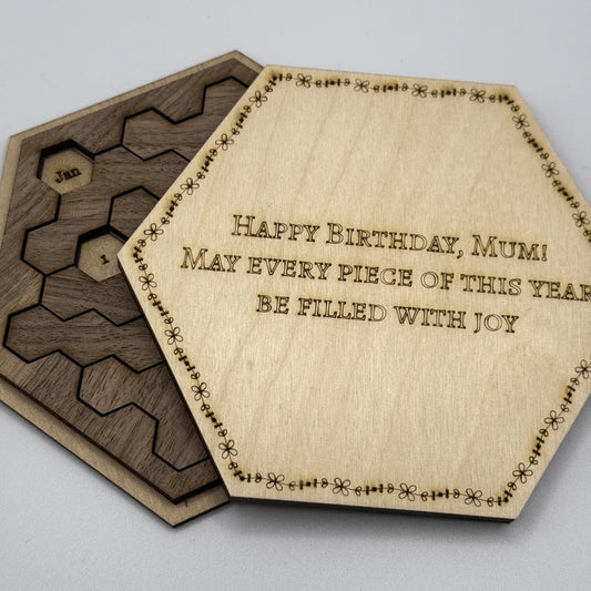 The image shows a Hexagon Calendar Puzzle Gift Edition featuring wooden tiles arranged in a hexagonal shape and inscribed with "Happy Birthday, Mum!