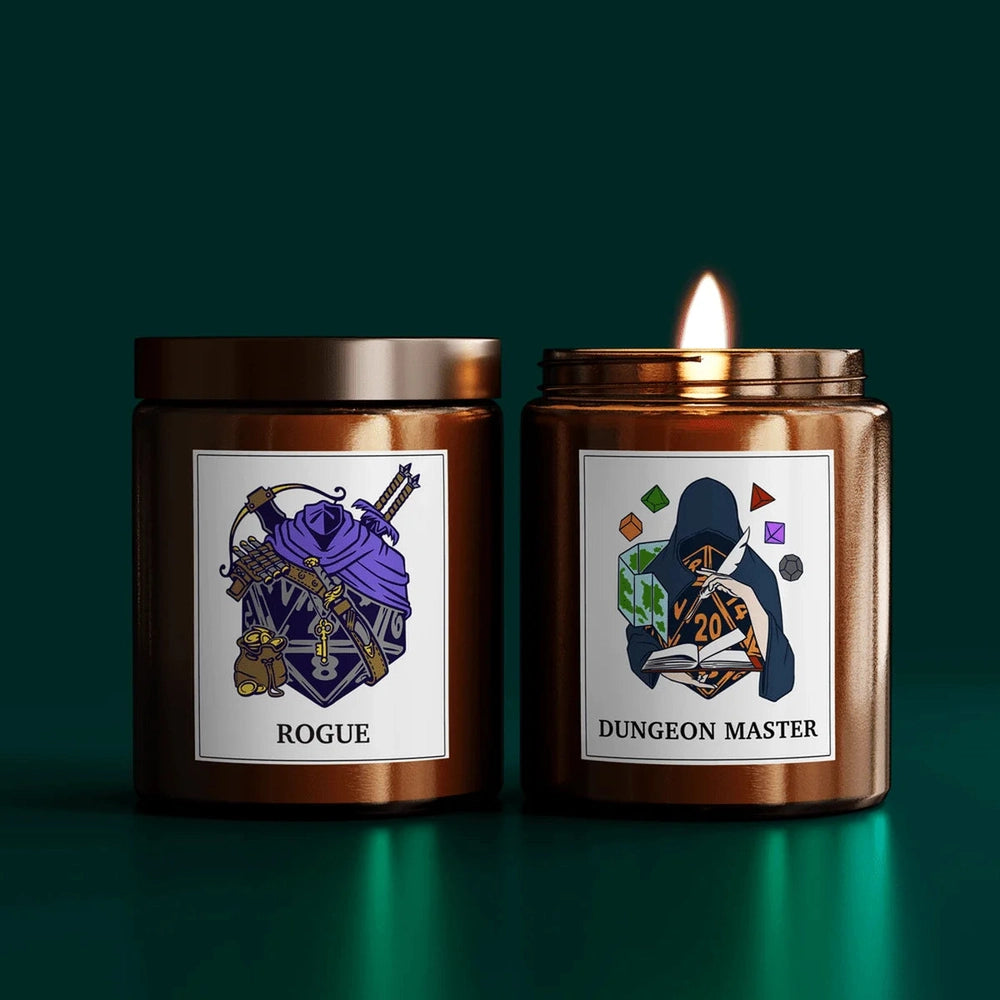 Two DnD scented candles are displayed side-by-side, one labeled "Rogue" and the other "Dungeon Master," each featuring custom illustrations on their lids.