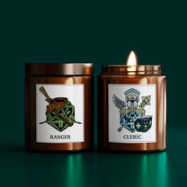 Two DnD scented candles are displayed side-by-side, one labeled "Ranger" featuring an illustration of a bow and die, and the other labeled “Cleric” displaying a winged emblem and die.