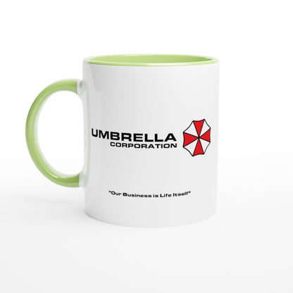 A white mug features a green rim and handle, displaying the Umbrella Corporation logo and the phrase "Our Business is Life Itself" referencing the Resident Evil series.