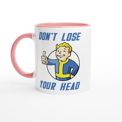 A white mug with a pink handle features Vault-Tec branding and cartoon graphics reading "Don't Lose Your Head" referencing the Fallout video game series.