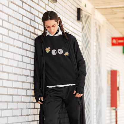 A person wearing a black Soot Sprites embroidered hoodie inspired by Studio Ghibli, layered under a white shirt and long black coat, stands against a brick wall.