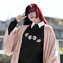 A person wearing a black Soot Sprites embroidered sweater inspired by Studio Ghibli poses outdoors with one hand raised in a peace sign.