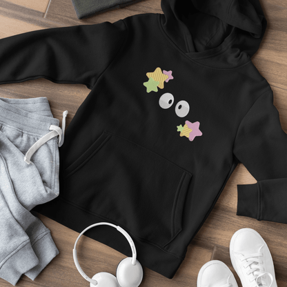 A black Soot Sprites embroidered hoodie, inspired by Studio Ghibli, is laid out on a wooden surface with matching sweatpants and sneakers.