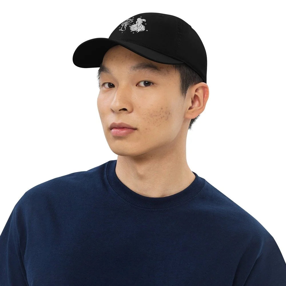 A person wearing a black Jujutsu Kaisen embroidered baseball cap featuring a betta fish and yin yang symbol design.