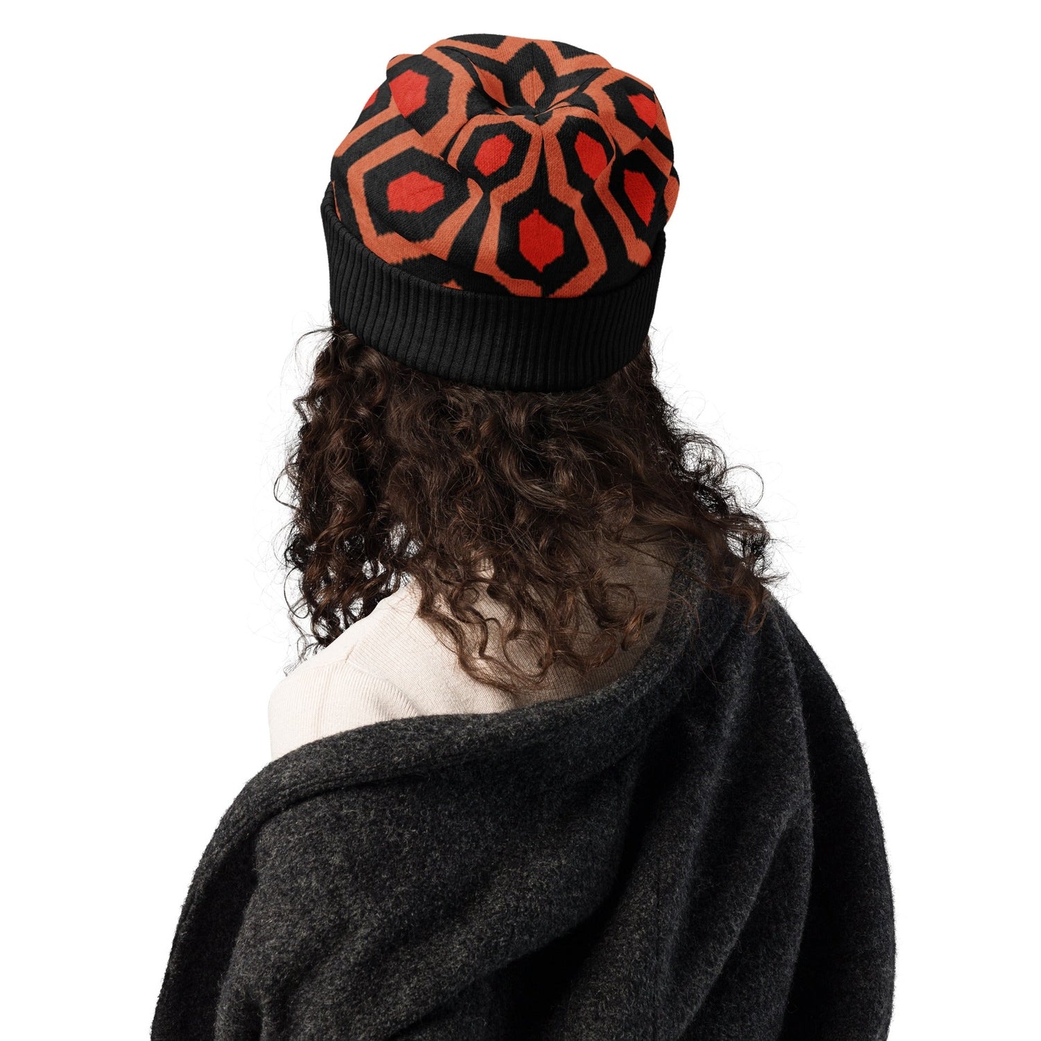 Person wearing an Overlook Hotel carpet pattern knitted beanie in orange, black and red on a white background