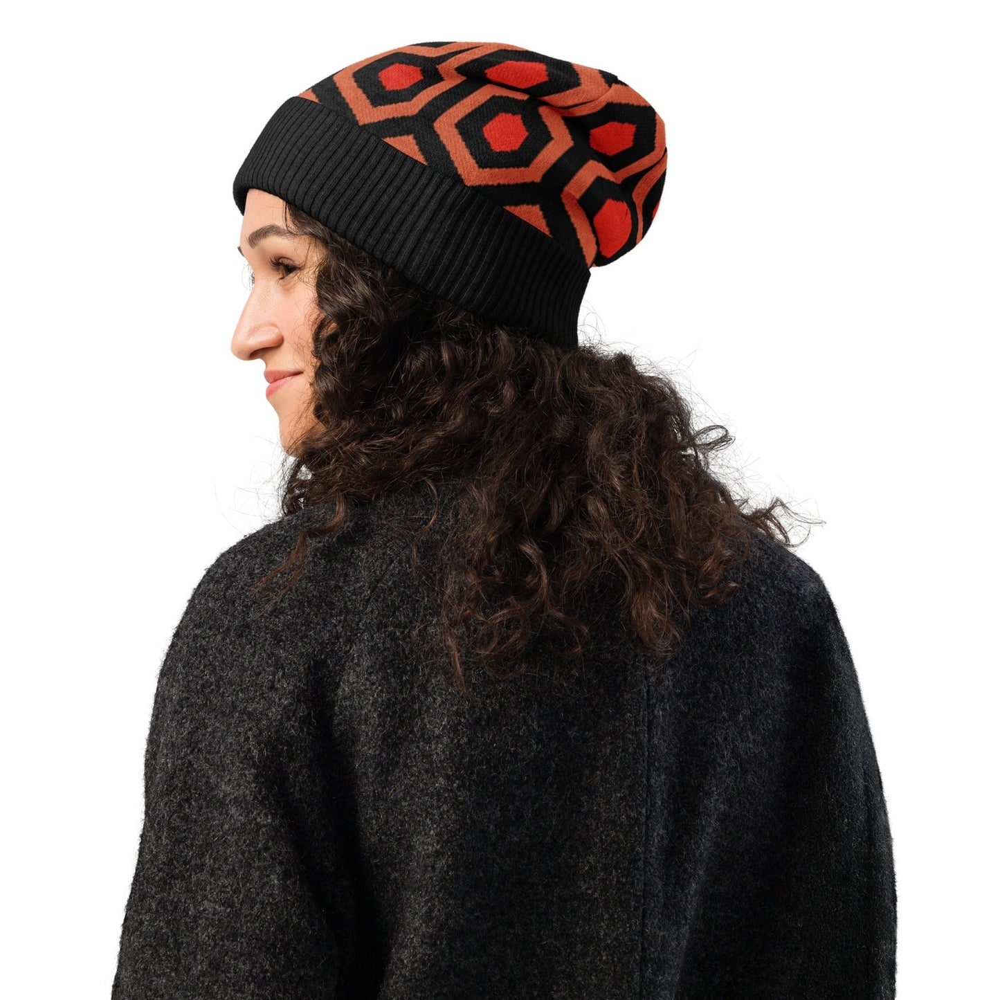Person wearing an Overlook Hotel carpet pattern knitted beanie in orange, black and red on a white background