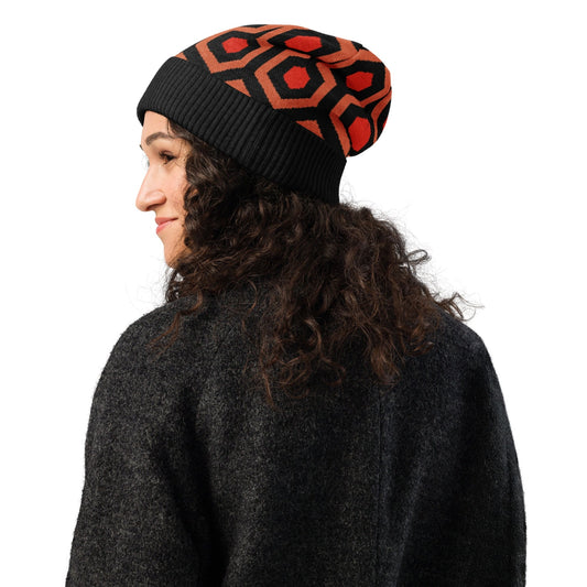 Person wearing an Overlook Hotel carpet pattern knitted beanie in orange, black and red on a white background