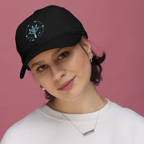 A person wearing a black Zelda Sheikah embroidered cap featuring a glowing eye design from Tears of the Kingdom.