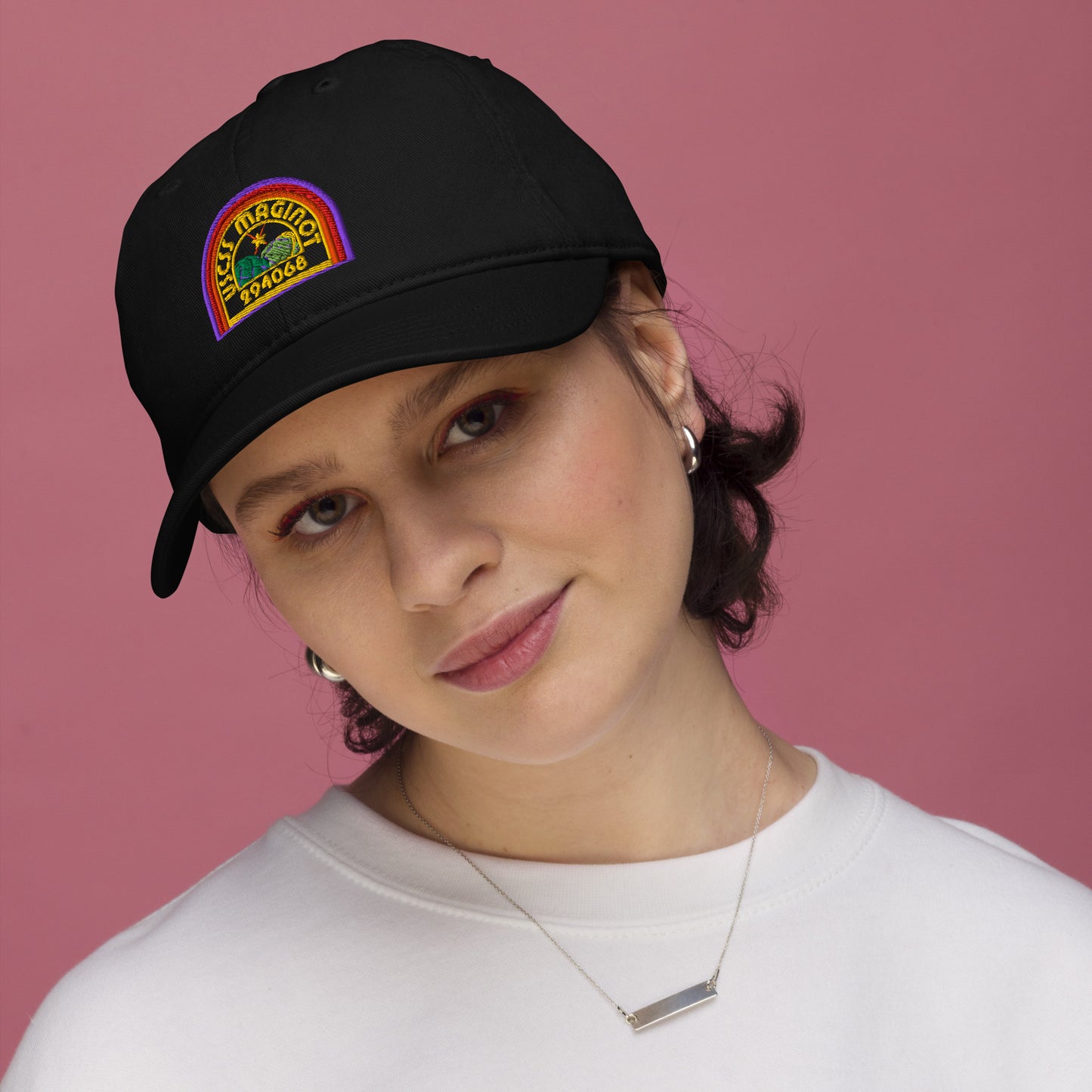 A person wearing a black Alien USCSS Maginot embroidered logo baseball cap with rainbow detailing.