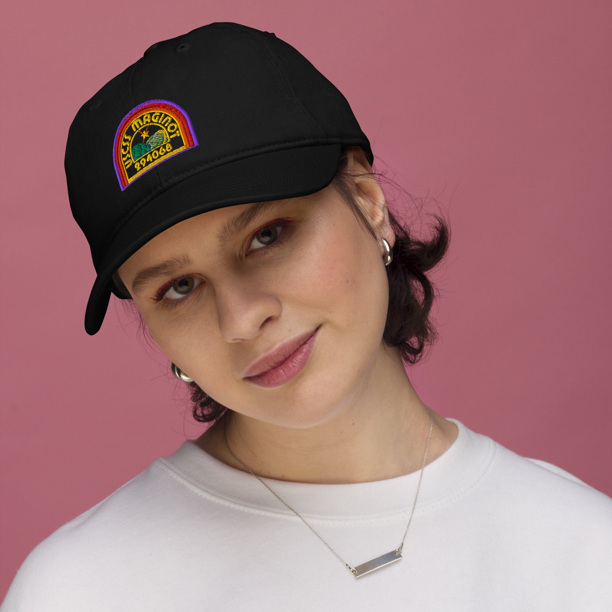 A person wearing a black Alien USCSS Maginot embroidered logo baseball cap with rainbow detailing.