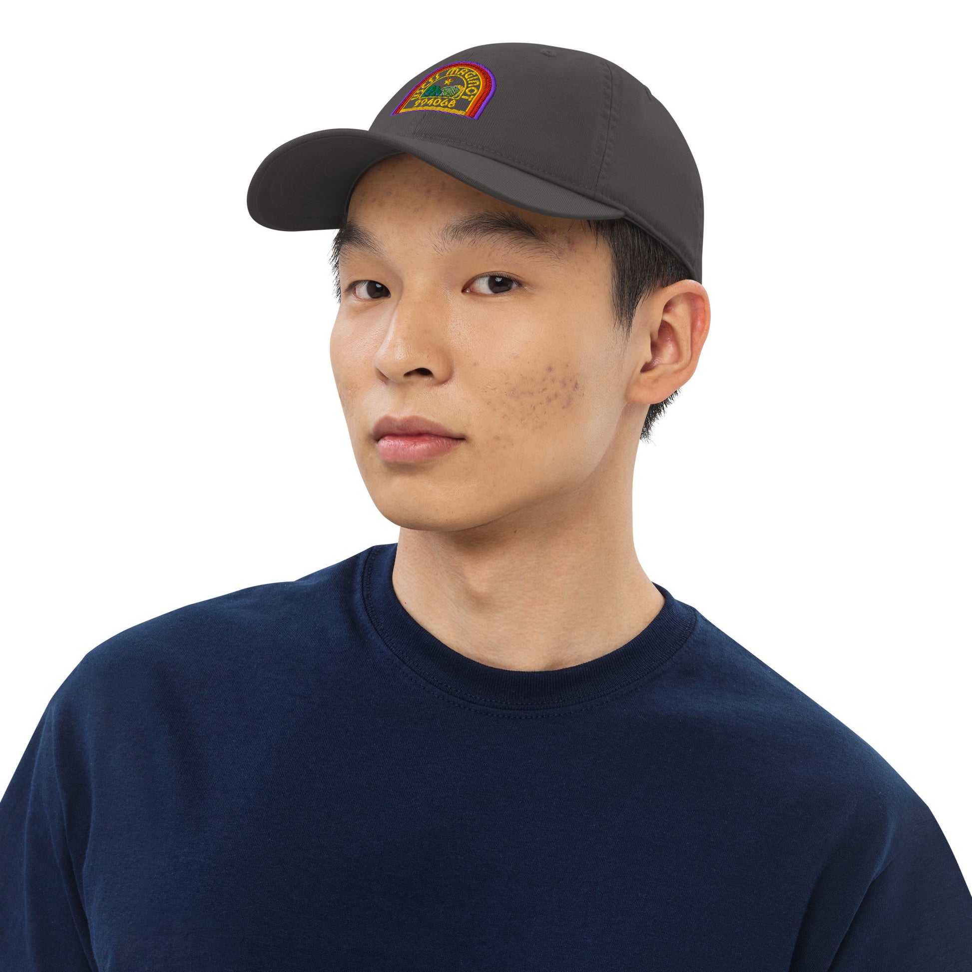 A person wearing a gray Alien USCSS Maginot embroidered logo baseball cap with rainbow-colored lettering on the front.