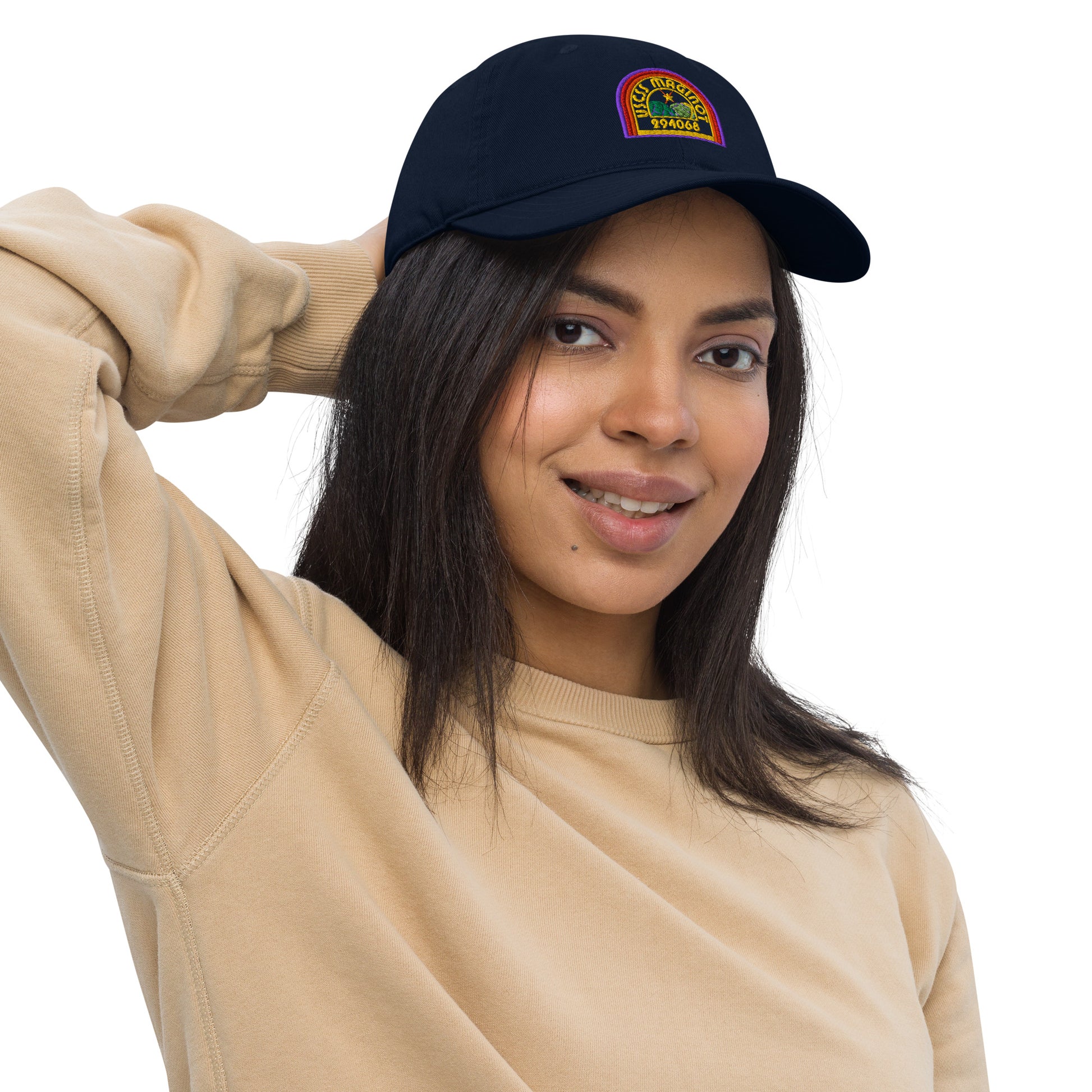 A person wearing a navy blue baseball cap featuring an embroidered logo that reads "USCS Maginot" in rainbow colors.
