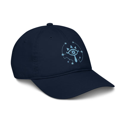 A navy blue dad hat features an embroidered Sheikah eye design from The Legend of Zelda: Tears of the Kingdom that glows in the dark.