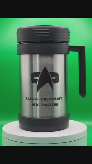 A silver travel mug that resembles a thermos spins slowly against a green background. The design features the Star Trek delta shield logo and "U.S.S. Defiant NX 74205" printed on its surface