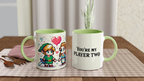 A pair of ceramic mugs features pixel art depicting Link and Zelda from The Legend of Zelda, along with the phrase "You're My Player Two.