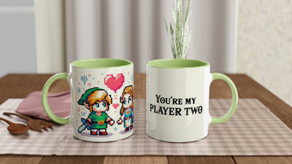 A pair of ceramic mugs features pixel art depicting Link and Zelda from The Legend of Zelda, along with the phrase "You're My Player Two.