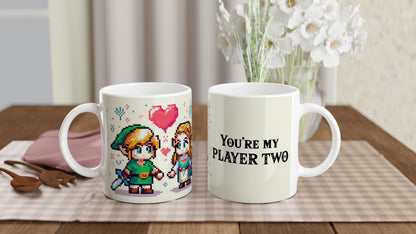 A white mug displays pixel art of Link and Zelda from The Legend of Zelda, along with the text "You're My Player Two.