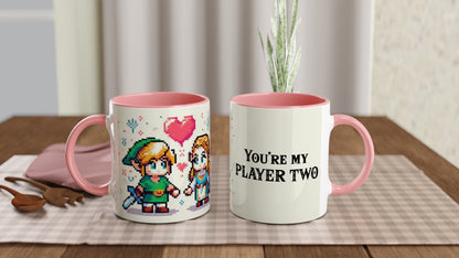 A white mug with a pink handle features pixel art of Link and Zelda from The Legend of Zelda, along with the words "You're My Player Two.