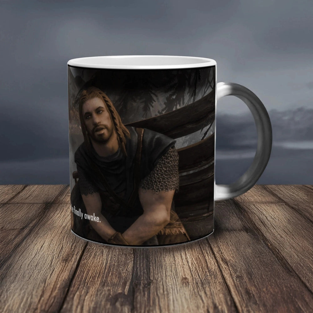 A white ceramic mug featuring a character from Skyrim and the text You're finally awake sitting on a wooden surface.
