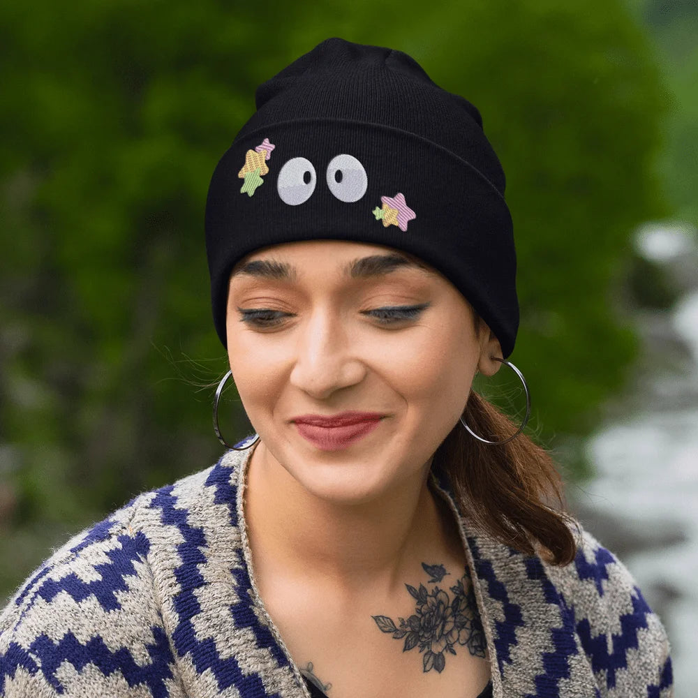 A person wearing a black Soot Sprites beanie featuring embroidered Susuwatari and star designs.