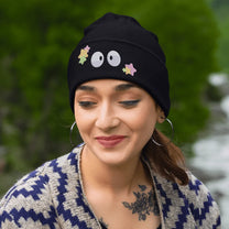 A person wearing a black Soot Sprites beanie featuring embroidered Susuwatari and star designs.