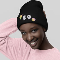 A person wearing a black Soot Sprites beanie featuring embroidered Susuwatari and star designs inspired by Ghibli.