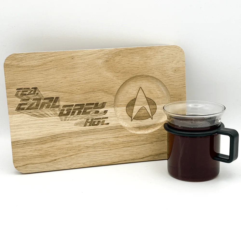 A wooden chopping board displays "Tea, Earl Grey, Hot" lettering and the Starfleet delta logo, next to a mug of dark tea.