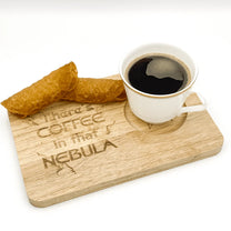 A wooden Voyager breakfast board displays a cup of coffee and a pastry, featuring the inscription "There's Coffee in that Nebula.